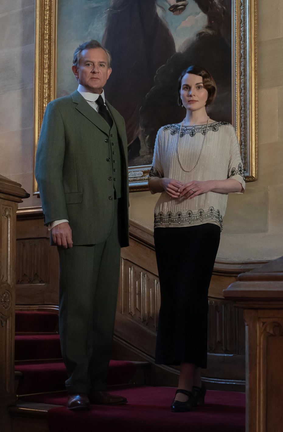 Hugh Bonneville as Robert Grantham AND Michelle Dockery as Lady Mary standing on the main stairwell of Downton Abbey